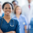 A smiling nurse stand with other nurses and professionals in the background.