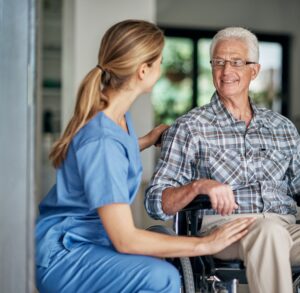 Light Housekeeping in Bowie A woman care giver with blond hair on bent knee places arm on shoulder of a cheerful elderly patient in a wheel chair. Light Housekeeping in Bowie