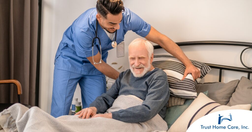 A home health care worker helps a patient in bed while both smile representing the results of a safe work habits.