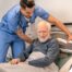 A home health care worker helps a patient in bed while both smile representing the results of a safe work habits.