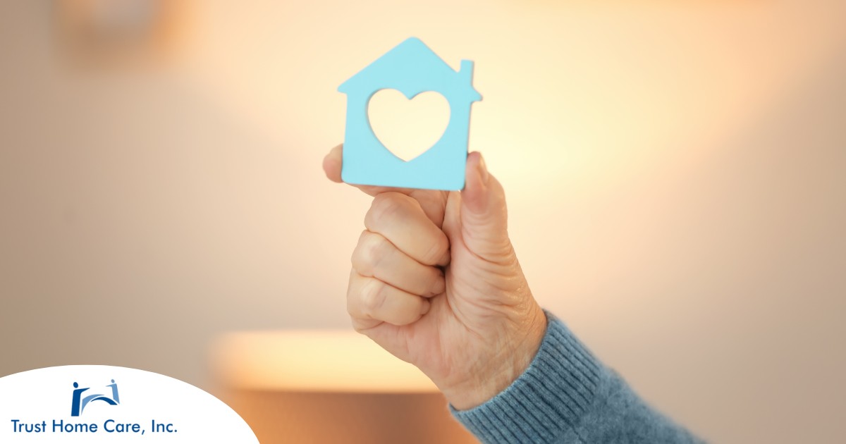 A hand holds up a cutout of a home with a heart in it, representing the home care industry.