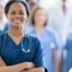 A woman in scrubs with a healthcare team behind her represents starting a new home health care job with a confident approach.
