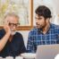 A man looks at a computer with his father who is confused, representing one of the early signs of dementia.