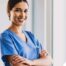 A woman in scrubs smiles representing the satisfaction of finding out how to become a home health aide.