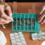 Older hands organize pills into a pill organizer, showing a great tool for managing medications.